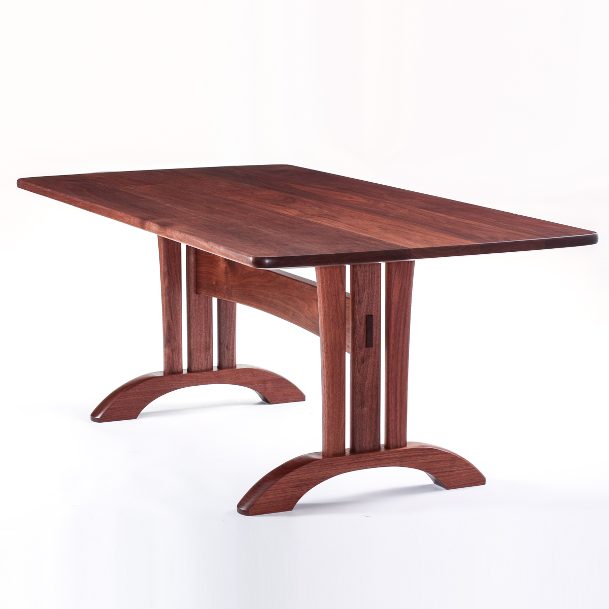 A quarter view of our Mitchell Trestle Table in walnut, in our studio.  The structure of this base is sculpture.