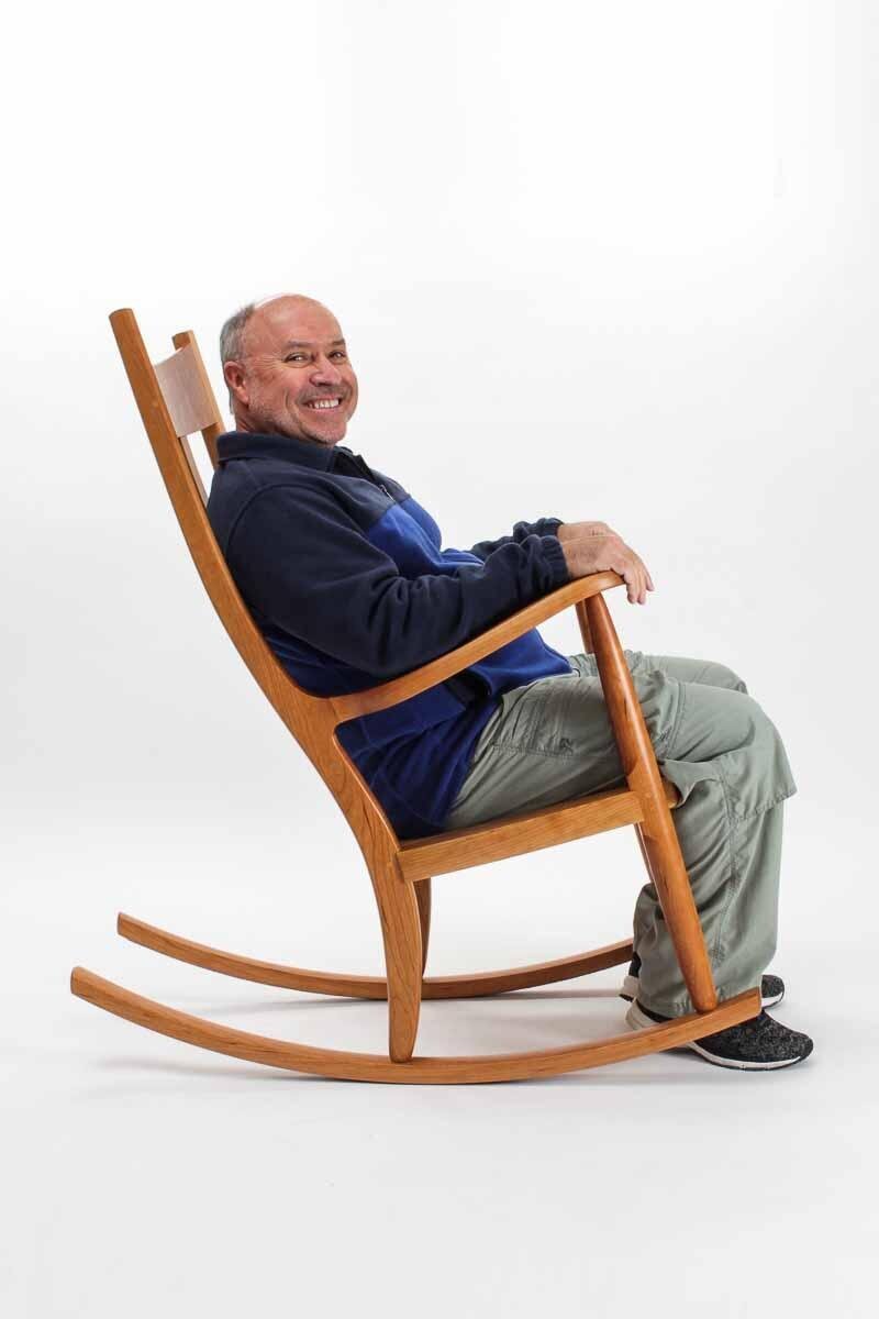 A side view of man grinning and rocking in a Weeks Rocker®.  The chair arms and back follow and fit the curve of his body.